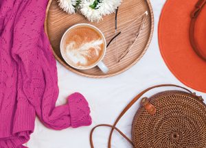 latte coffee on tray with flowers and eye glasses, sweater, purse and hat